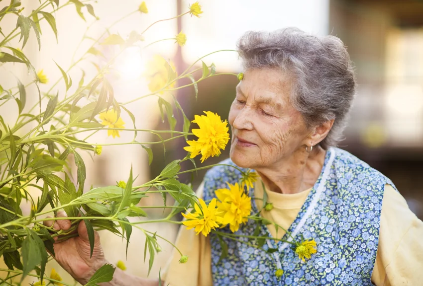 An older woman smelling flowers to show Blossom's award-winning care services.