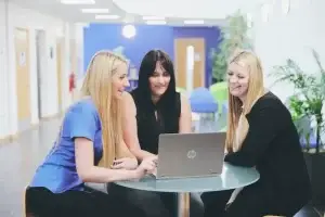 3 Blossom carers at a table around a laptop to show care worker's week.