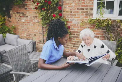 A Blossom home carer reads a book with a client outdoors.