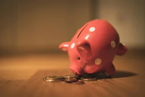 A pink piggy bank, leaning face down into some coins.