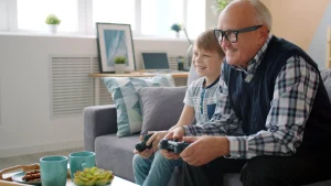 A grandfather and grandson hold video game console controllers.