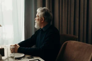 An elderly man sits gazing out of a window, deep in thought.